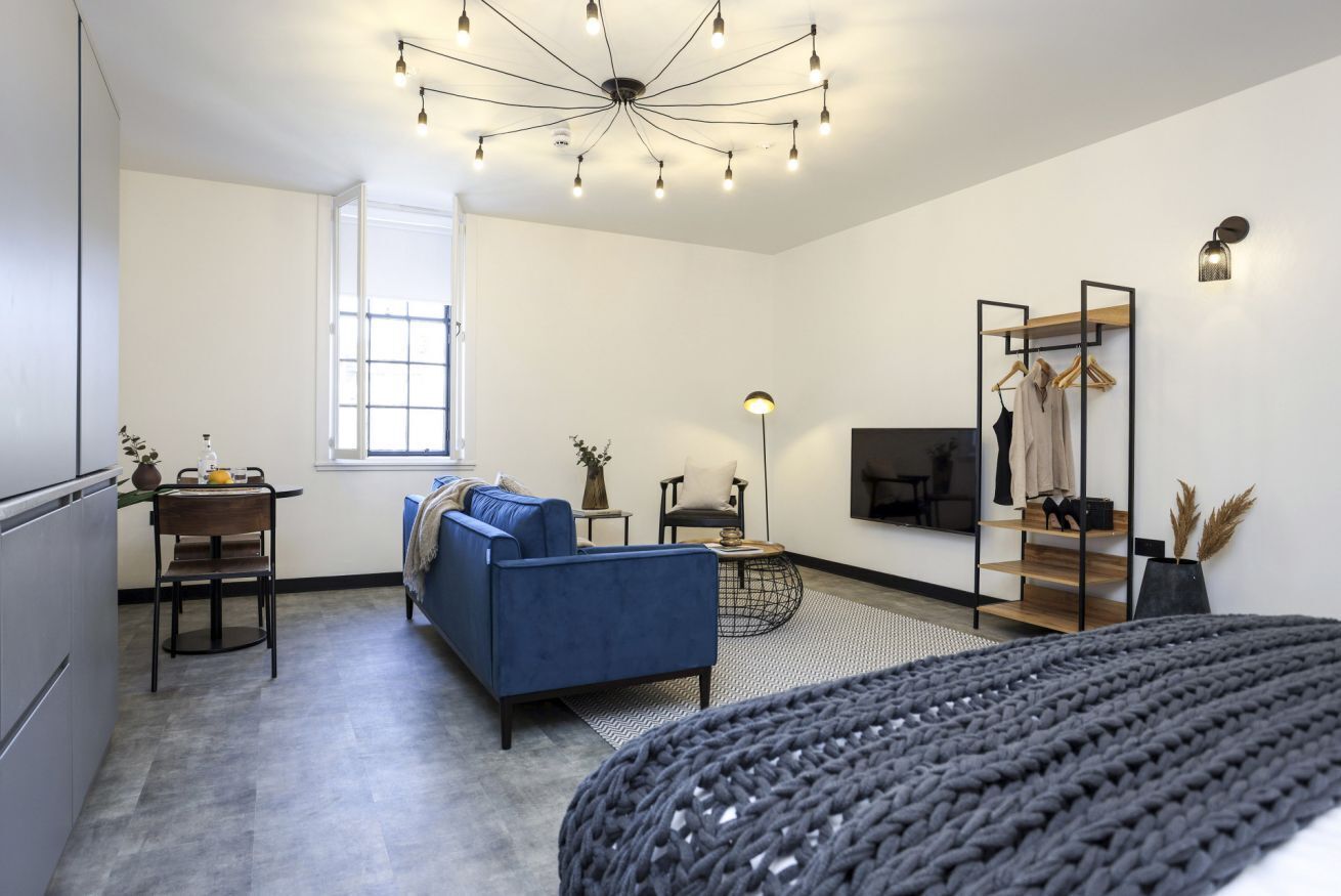 A modern living room with a blue sofa, a round coffee table, a TV mounted on the wall, and a clothing rack.