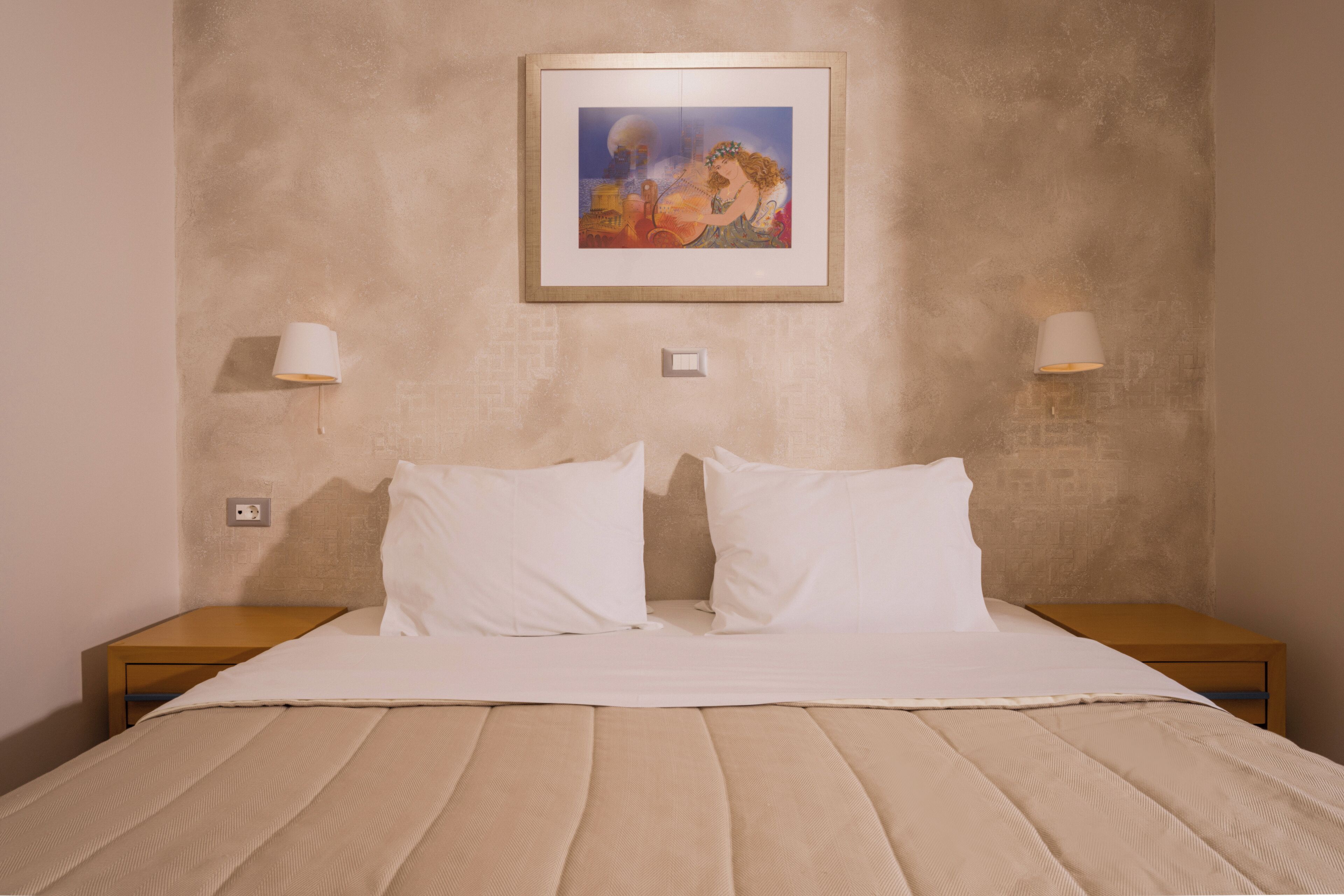 A neatly made bed with white linens, two bedside lamps, and a framed picture on the wall.