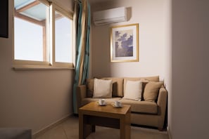 A room with a sofa, a small table with cups, a window with curtains, an air conditioner, and a framed picture on the wall. - Plaza Hotel (Zakynthos)