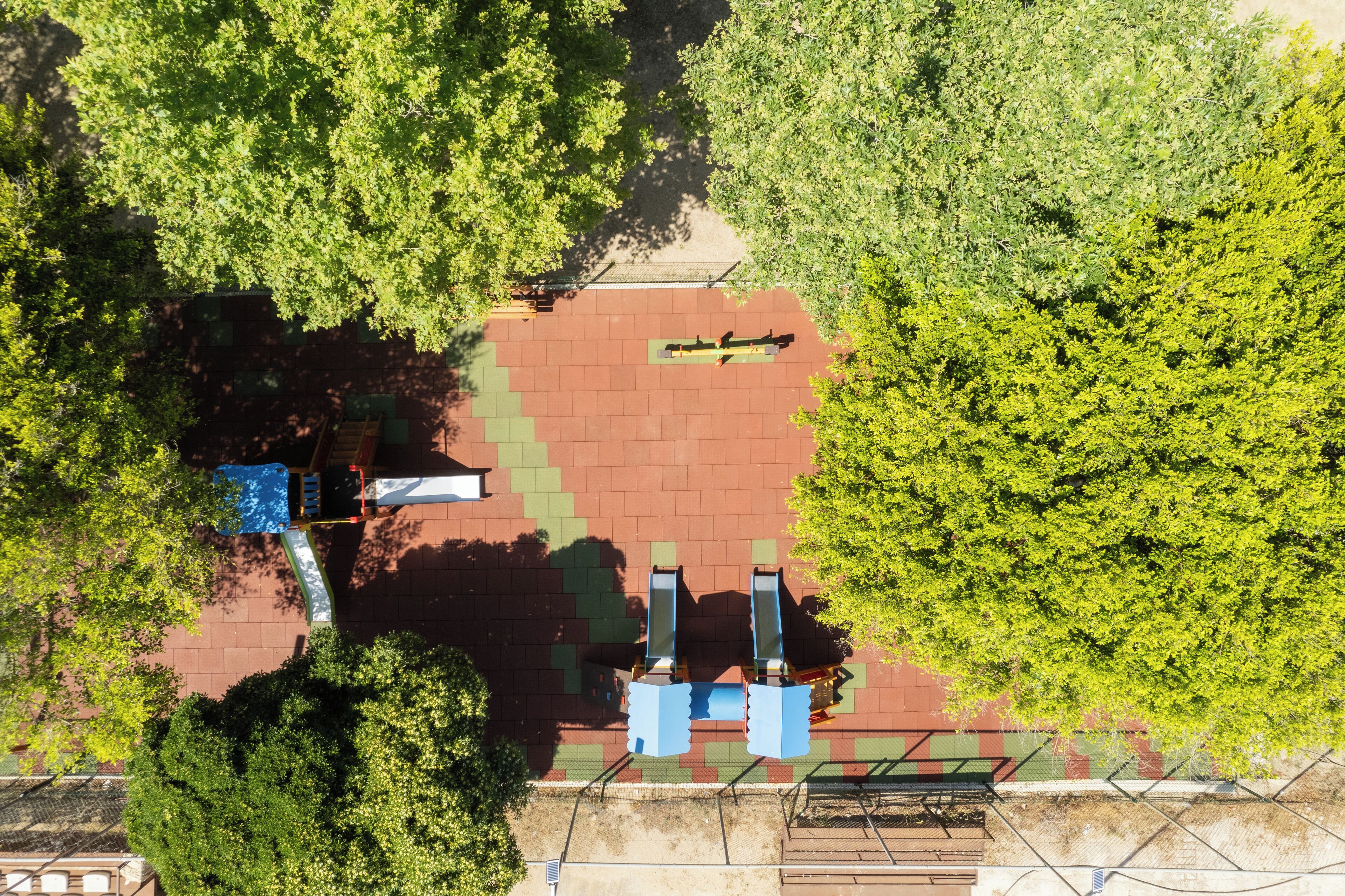 An aerial view of a park with a red brick area, green trees, and a blue bench.