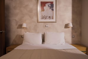 A bedroom with a bed, two bedside lamps, a framed artwork on the wall, and a nightstand. - Plaza Hotel (Zakynthos)