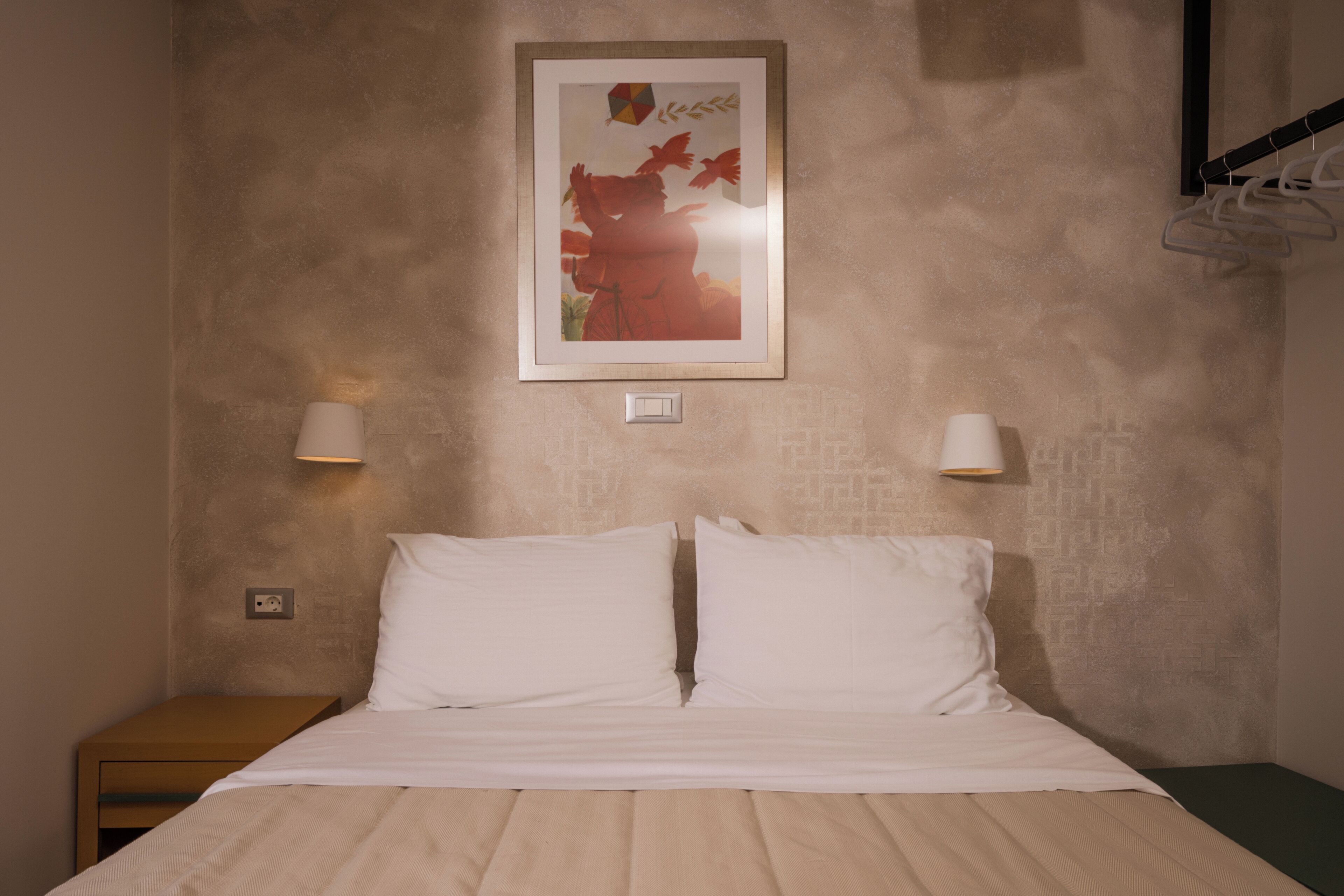 Una cama bien hecha con sábanas blancas, dos lámparas de noche y un cuadro en la pared.