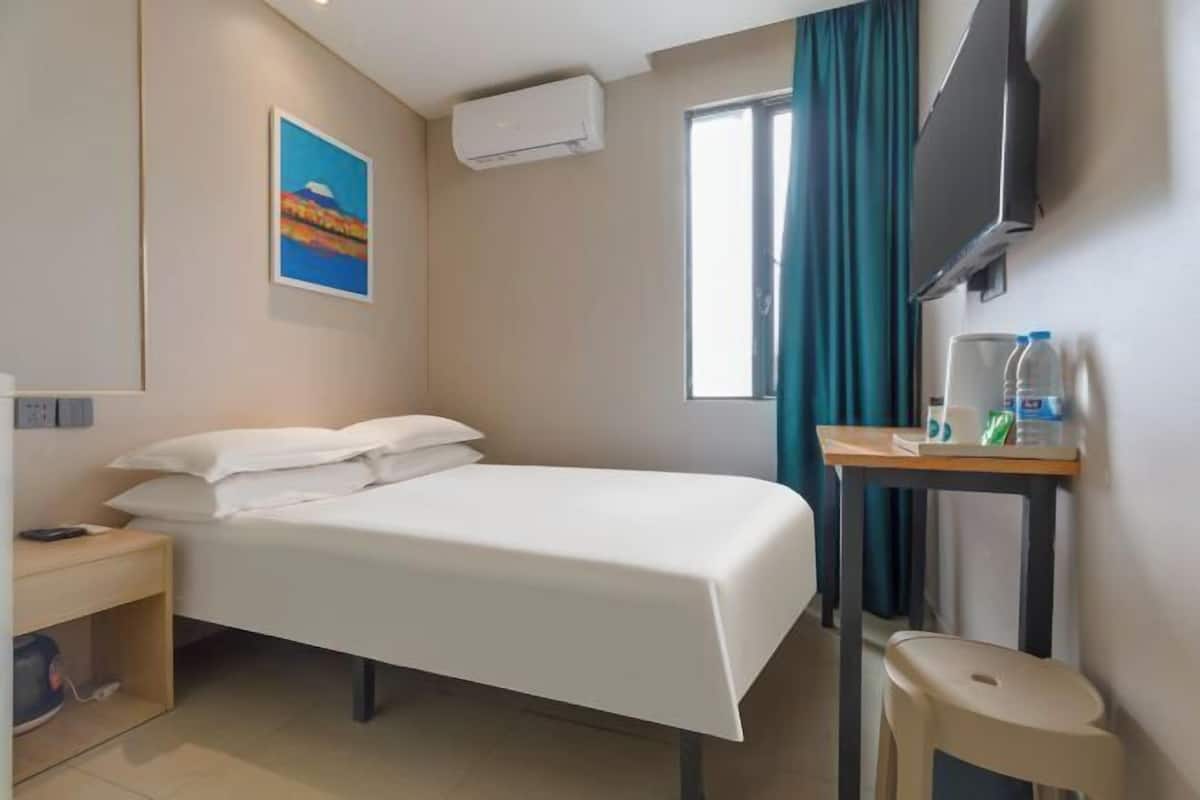A hotel room with a bed, a desk, a chair, a TV, and a window with curtains.