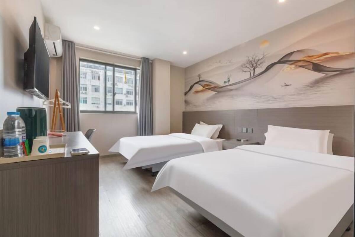 A hotel room with two beds, a desk, a TV, and a large window.