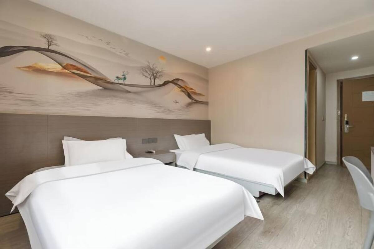 A hotel room with two beds, a modern mural on the wall, and a wooden floor.
