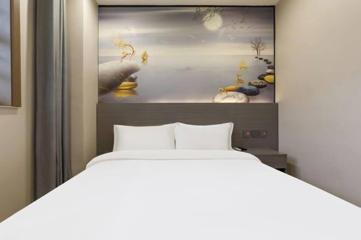 A bedroom with a bed, a nightstand, and a wall-mounted artwork depicting a serene landscape.