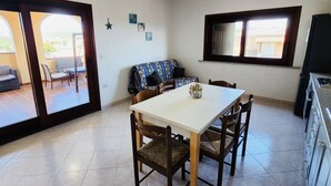 Un comedor con una mesa blanca y sillas de madera, un sofá azul estampado y una ventana con vistas.