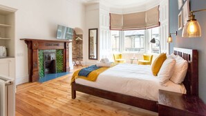 A bedroom with a large bed, a fireplace, a window with a view, and a small table with chairs.