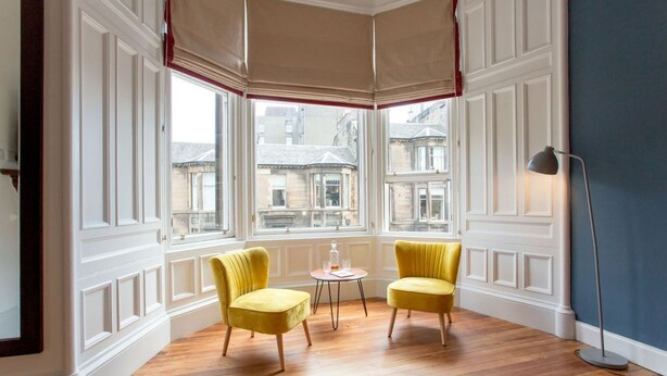 A corner room with two yellow chairs, a small round table, and a floor lamp.