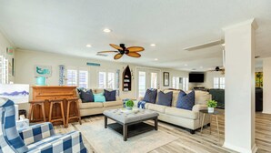 A spacious living room with a large sofa, a coffee table, and a dining area. - Seabreeze Oasis - Beachy Days, Starry Nights! (Surfside Beach)