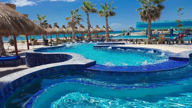 Un área de piscina con varias fuentes, palmeras y sillas de descanso.