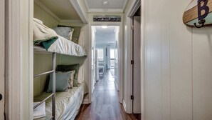 A narrow hallway with bunk beds on one side and a door with a surfboard decoration on the other. - Drifty Daze Oceanfront Suite w Pool (North Myrtle Beach)