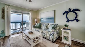 A living room with a sofa, a coffee table, a small side table, a ceiling fan, and a view of the ocean through a sliding glass door. - Drifty Daze Oceanfront Suite w Pool (North Myrtle Beach)