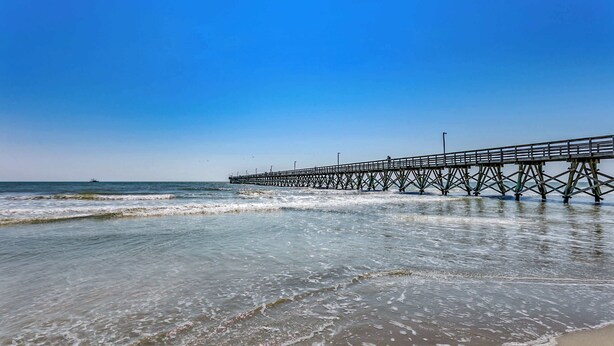 A pier extending into the ocean with clear skies above. - Drifty Daze Oceanfront Suite w Pool (North Myrtle Beach)