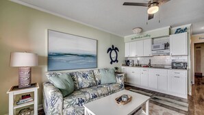 A living room with a sofa, a coffee table, a lamp, and a painting on the wall. - Drifty Daze Oceanfront Suite w Pool (North Myrtle Beach)