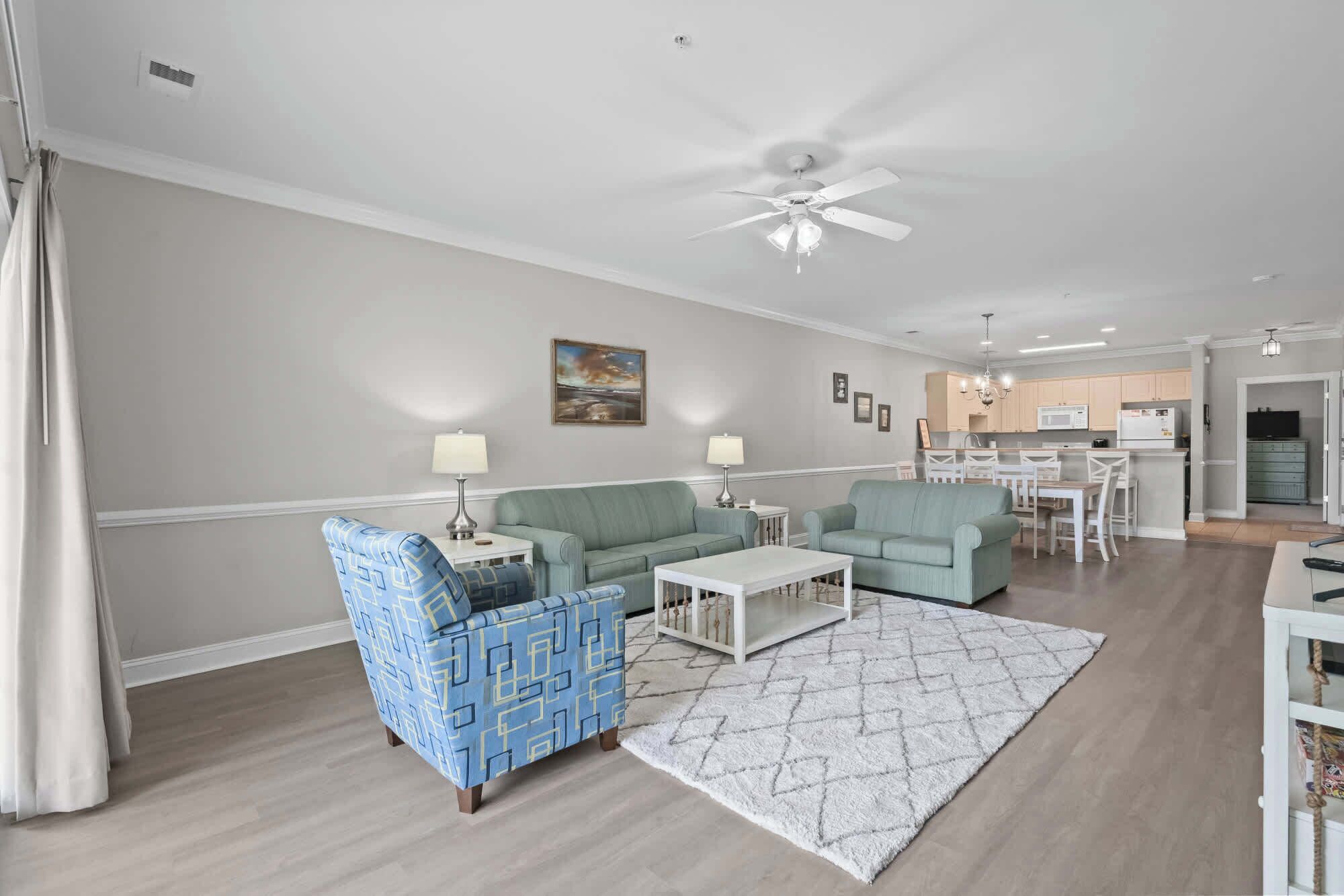 A modern living room with a sofa, armchairs, and a coffee table. There is a dining area with a table and chairs, and a kitchen in the background.