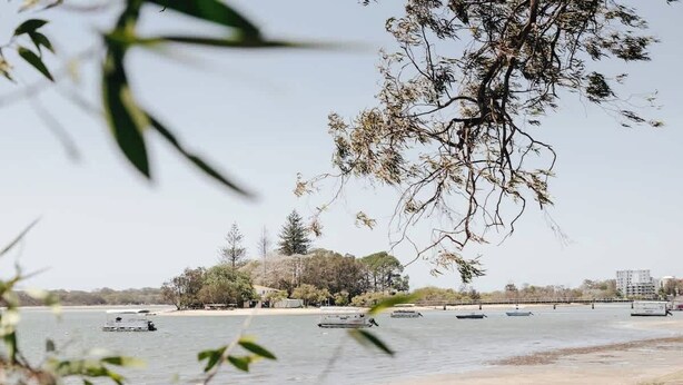 A calm river with boats, a sandy shore, and trees in the background.