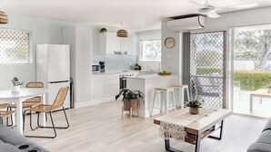 A modern kitchen with white cabinets, a dining area with a round table and chairs, and a large sliding glass door leading to an outdoor area.