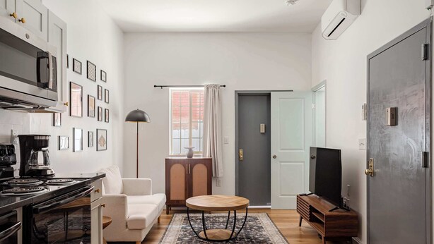 Un espacio habitable compacto con kitchenette, un sofá, una mesita redonda y un televisor.