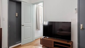 Una habitación con una televisión de pantalla grande en un soporte de madera, una puerta gris cerrada y una puerta blanca.