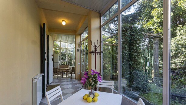 A sunlit room with a table set for two, a chair, and a view of greenery outside.