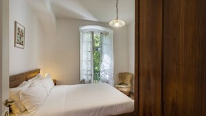 A bedroom with a wooden bed, a nightstand, a chair, and a window with curtains.