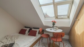 A small, well-lit room with a skylight, a bed, a table with chairs, and a radiator. - Backyard Design home near Castle  (Prague)