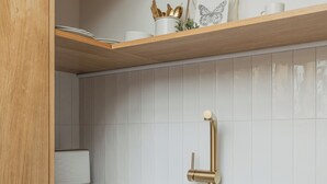 A modern kitchen with wooden shelves, a white tiled backsplash, and a gold faucet. - Backyard Design home near Castle  (Prague)
