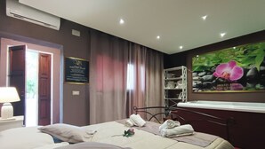 A hotel room with a bed, a chair, a shelf with towels, and a wall-mounted TV displaying an orchid. - villa di l'abbiu country relax (Sorso)