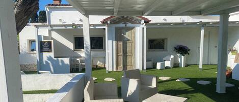 Un'area salotto esterna coperta con mobili in vimini bianco, un muro in pietra e una struttura a pergola.