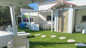 A covered outdoor area with artificial grass, white wicker furniture, and a play structure. - villa di l'abbiu country relax (Sorso)