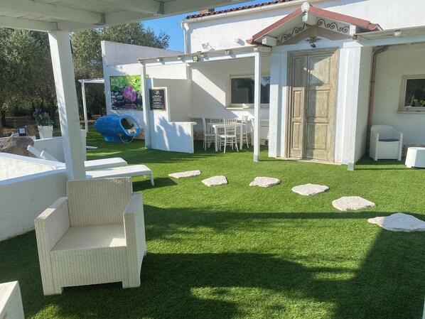 A covered outdoor area with artificial grass, white wicker furniture, and a play structure.