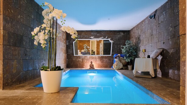 A serene indoor pool area with a clear blue pool, stone walls, and a Buddha statue. - villa di l'abbiu country relax (Sorso)