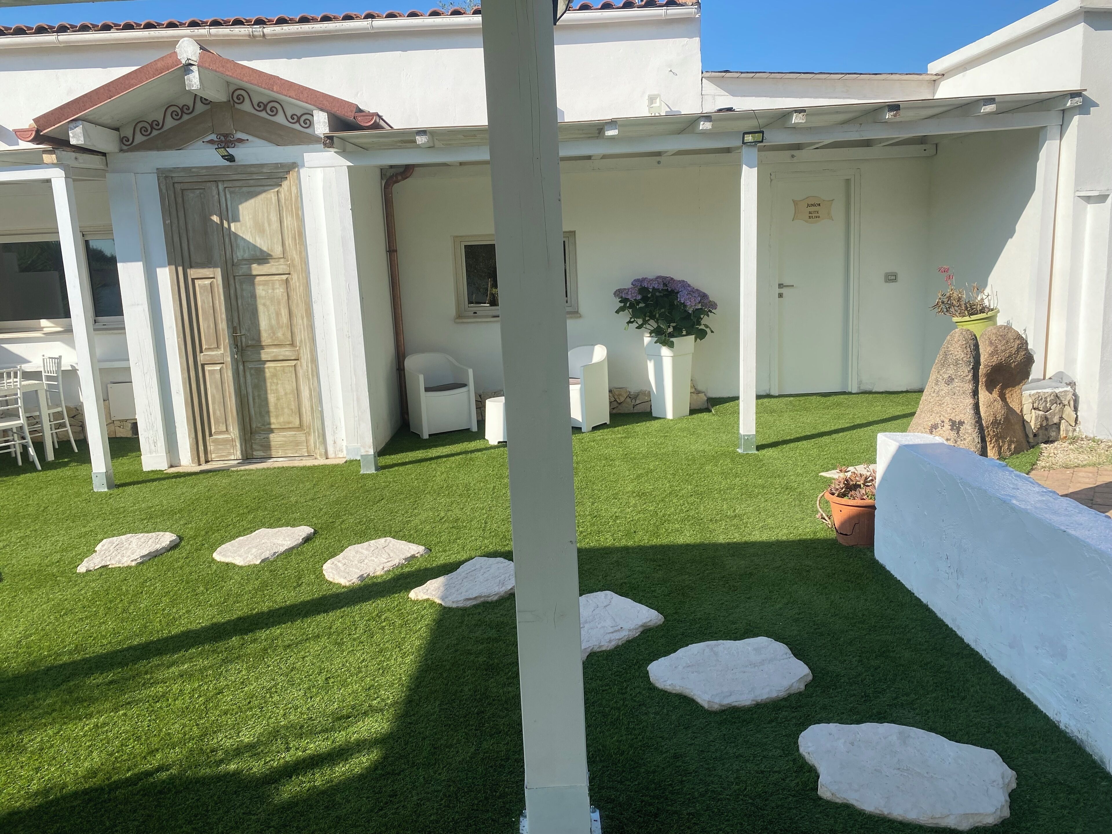 A patio area with artificial grass, white stone steps, and a white wall.