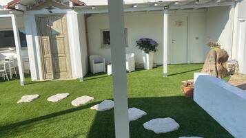 A patio area with artificial grass, white stone steps, and a white wall.