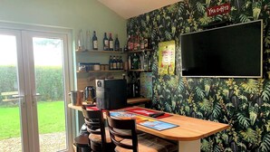 A bar area with a counter, chairs, and a TV screen. There are bottles and a menu on the wall.