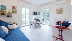 A modern living room with a blue sofa, a white couch, a dining table with chairs, and a small red table.