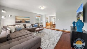 A modern living room with a sectional sofa, a round coffee table, and a white shag rug. There is a dining area with a wooden table and chairs, and a kitchen in the background. - Stylish Family Home Near Lake Geneva (Lake Geneva)