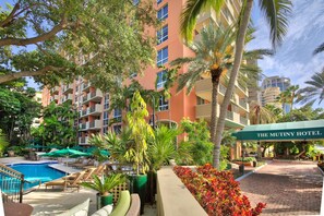 A hotel with a swimming pool, outdoor seating, and palm trees.