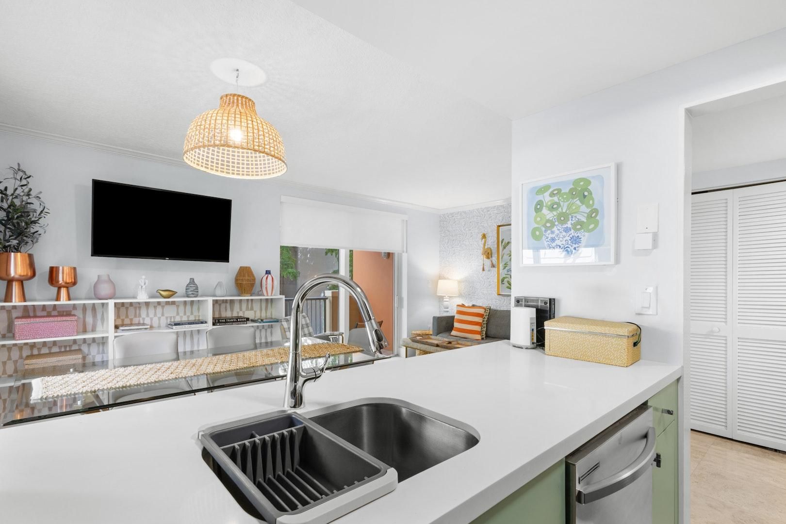 Eine moderne Küche mit integriertem Spülbecken, einer hängenden Pendelleuchte und einem an der Wand montierten Flachbildfernseher.