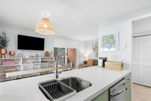 Une cuisine moderne dotée d’un évier encastré, d’une suspension lumineuse et d’un téléviseur à écran plat fixé au mur.