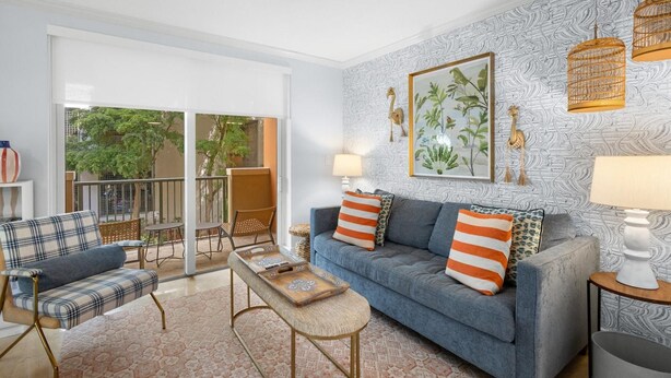 A living room with a sofa, armchairs, a coffee table, and a balcony with a view of greenery.