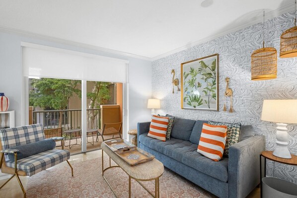 A living room with a sofa, armchairs, a coffee table, and a balcony with a view of greenery.