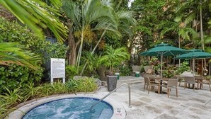 A hot tub surrounded by lush greenery, outdoor seating, and a sign with rules.