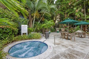 A hot tub surrounded by lush greenery, outdoor seating, and a sign with rules.