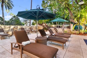 Un espace extérieur ensoleillé, aménagé avec des fauteuils confortables et des parasols, le tout entouré de verdure.