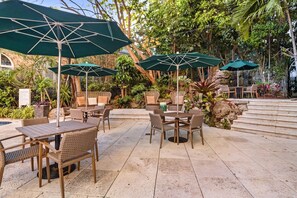 An outdoor patio area with multiple tables and chairs, some with green umbrellas.