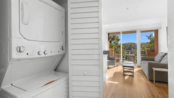 Ein moderner Waschraum mit integrierter Waschmaschine und Trockner, einer Schiebetür zu einem Balkon mit Gartenmöbeln und Blick ins Grüne.