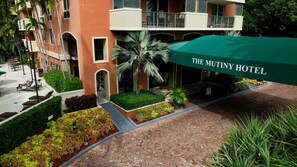 The Mutiny Hotel with a brick pathway, palm trees, and a green awning.