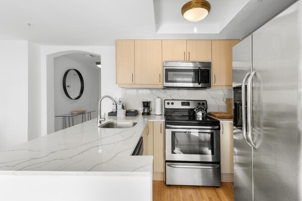 A modern kitchen with stainless steel appliances, wooden cabinets, and a marble countertop.